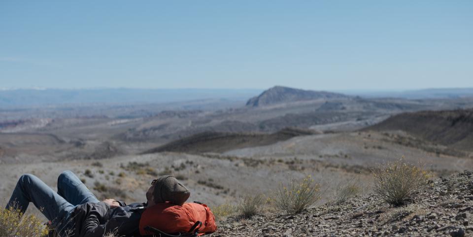 Man taking a nap with his head resting against an orange backpack.