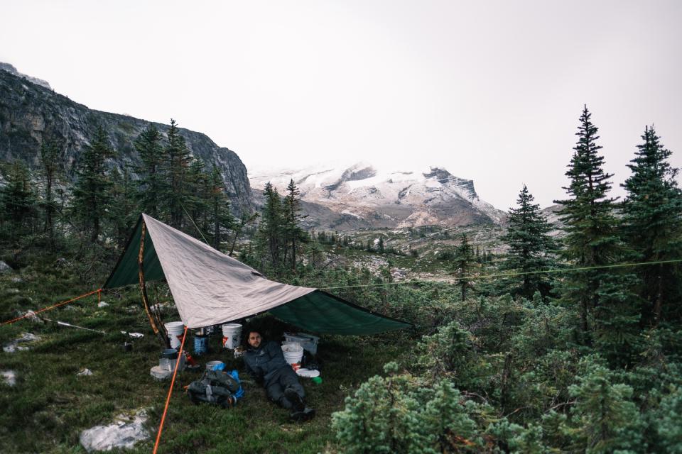 Man sitting under a tarp with a snow covered mountain in the background.