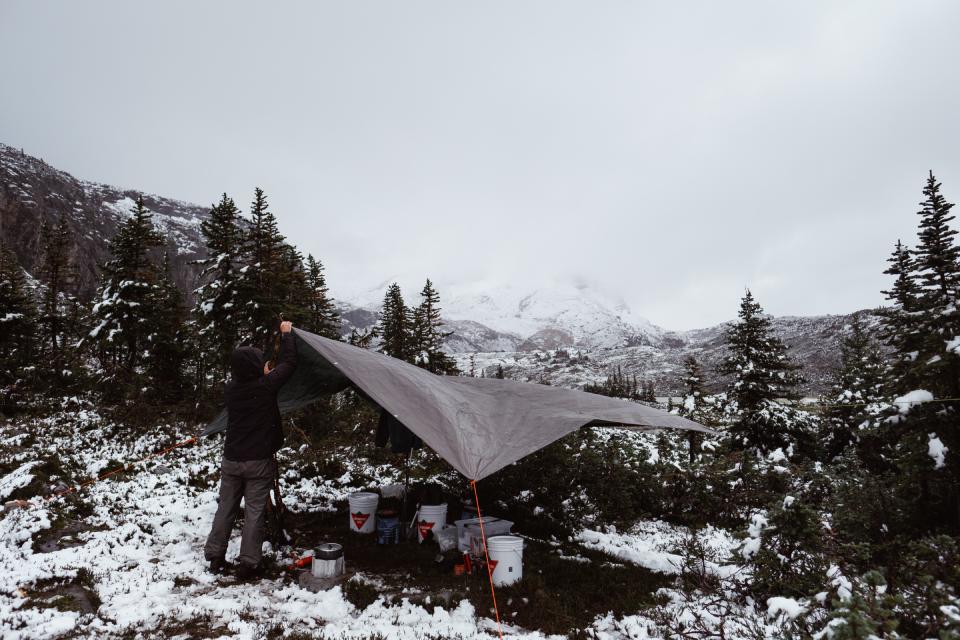 Man adjusting a tarp with a snowy landscape in the background.
