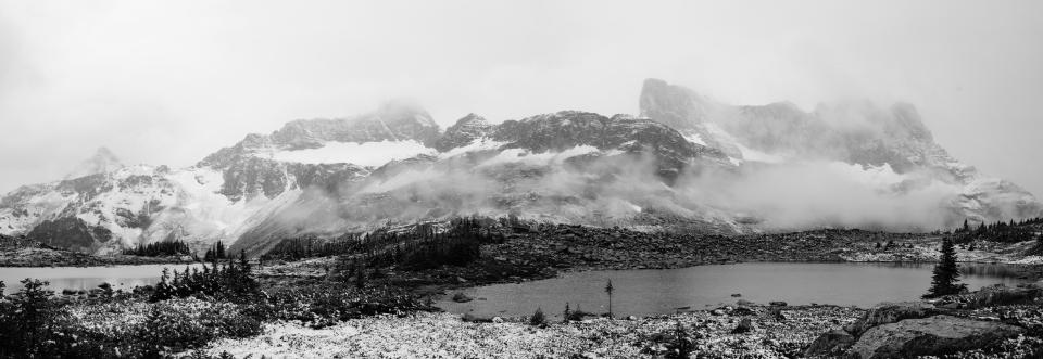 A black and white panorama showing a series of snow covered mountains.