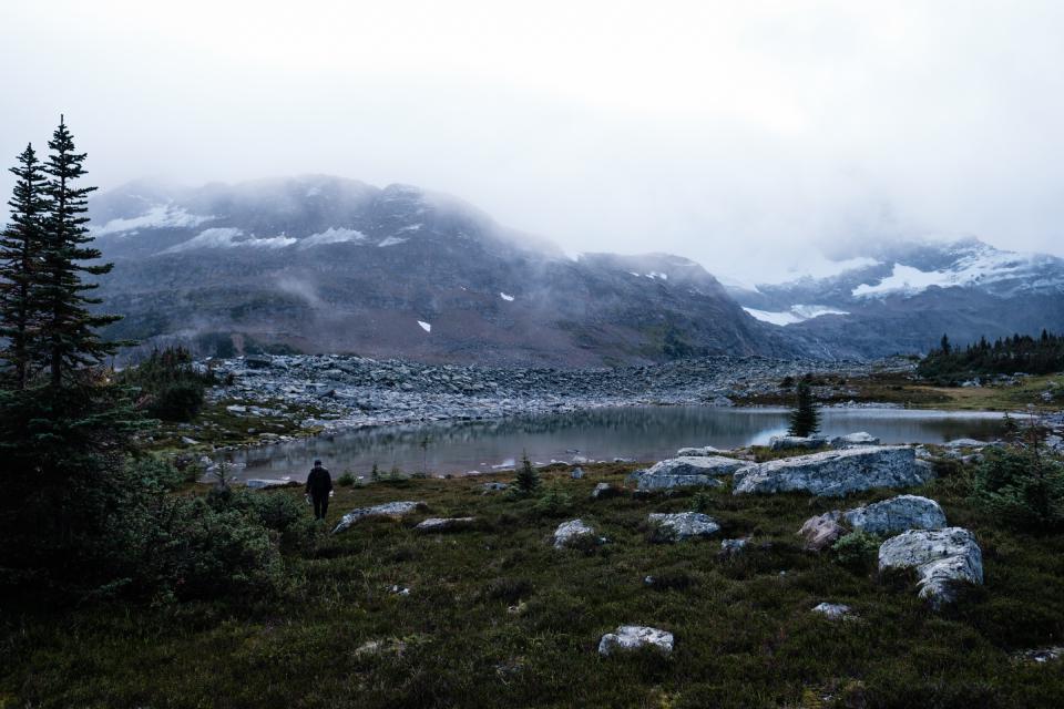 Man walking in an alpine meadow that is surrounded by clouds.